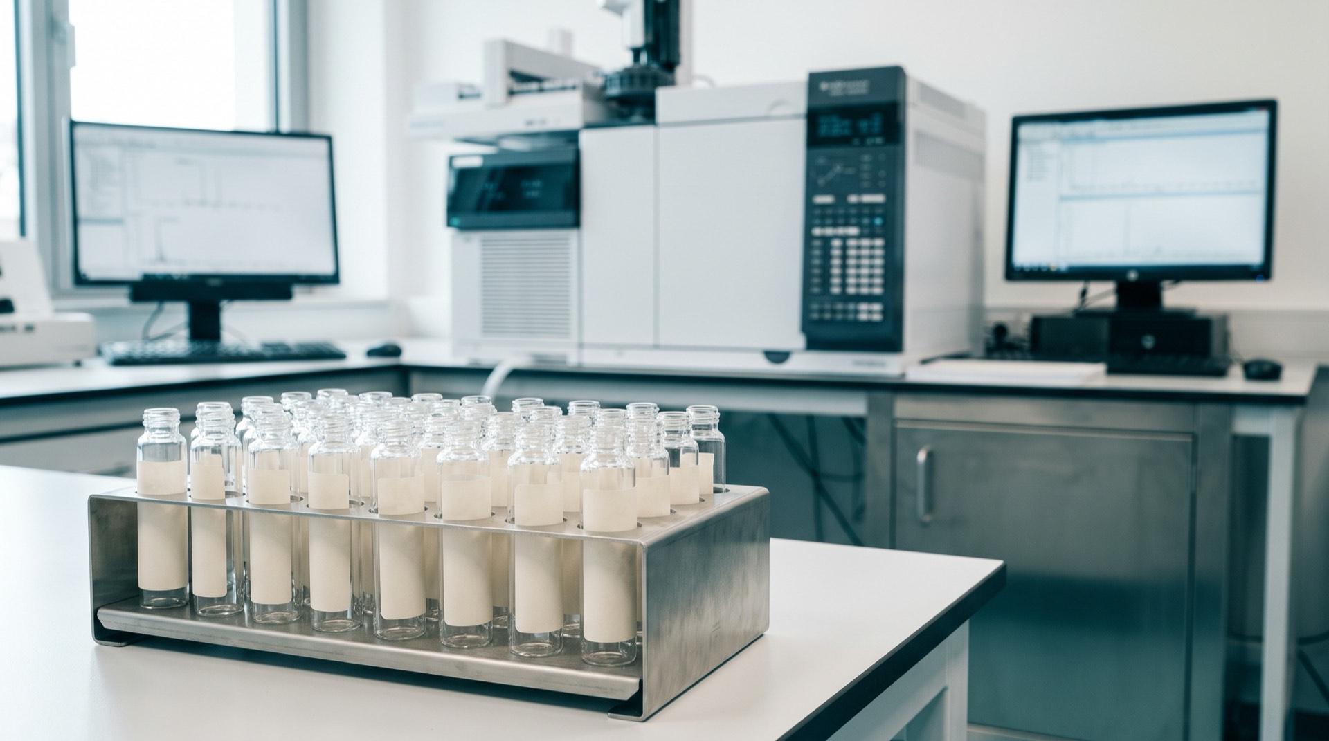 Rack of glass sample vials on a laboratory bench in front of analytical instruments